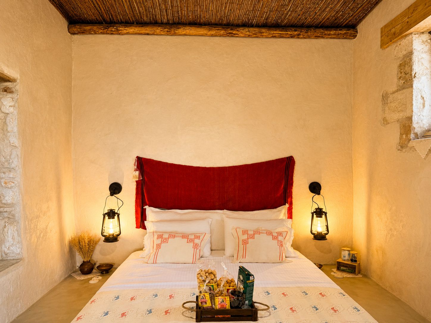 The bed with its red woven headboard between two lit lanterns
